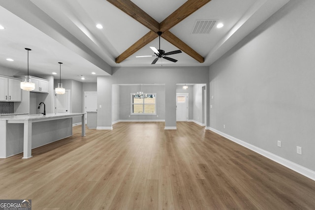 unfurnished living room with coffered ceiling, ceiling fan with notable chandelier, sink, light hardwood / wood-style floors, and beam ceiling