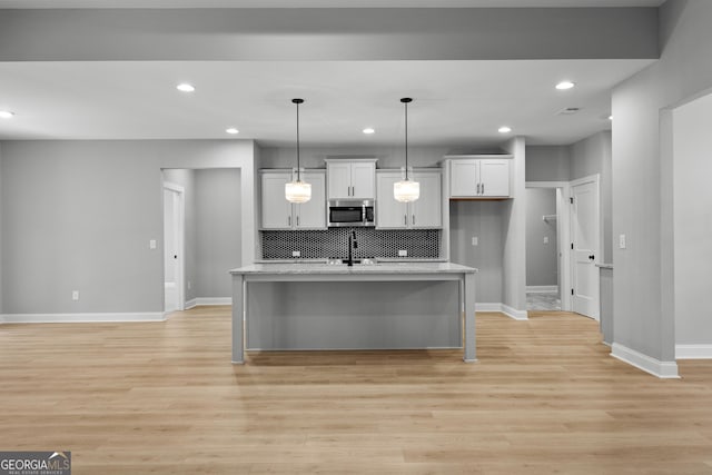 kitchen featuring light stone countertops, decorative light fixtures, light hardwood / wood-style flooring, and an island with sink