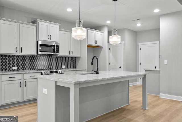 kitchen featuring pendant lighting, sink, light stone countertops, an island with sink, and light hardwood / wood-style floors