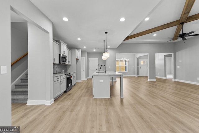 kitchen featuring stainless steel appliances, sink, beam ceiling, decorative light fixtures, and an island with sink