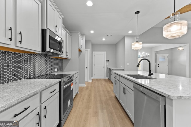 kitchen featuring a kitchen island with sink, hanging light fixtures, sink, decorative backsplash, and appliances with stainless steel finishes