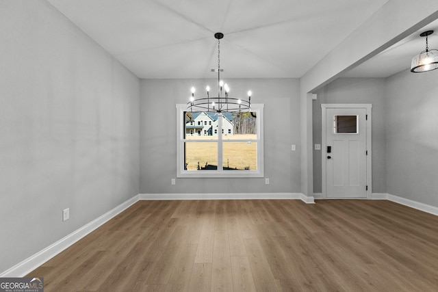 unfurnished dining area featuring wood-type flooring and an inviting chandelier