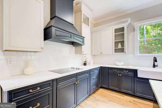 kitchen with white cabinets, light hardwood / wood-style flooring, custom range hood, black electric stovetop, and sink