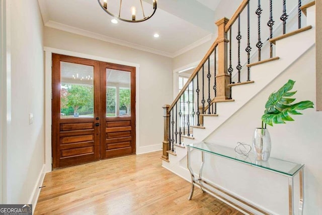 entryway featuring french doors, a notable chandelier, crown molding, and light wood-type flooring