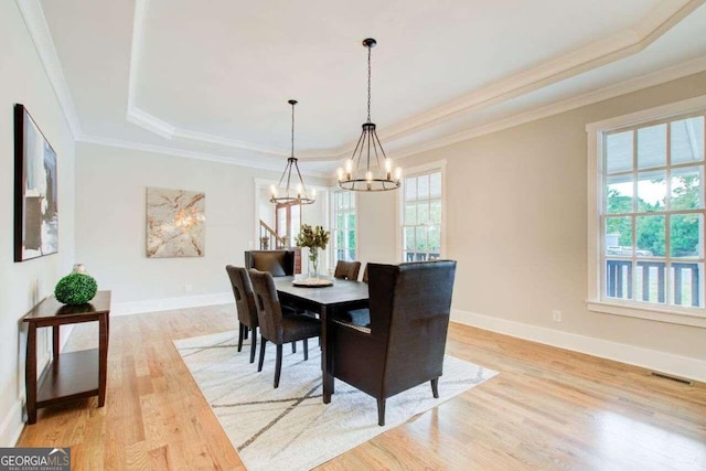 dining room with crown molding, light hardwood / wood-style flooring, a healthy amount of sunlight, and a raised ceiling