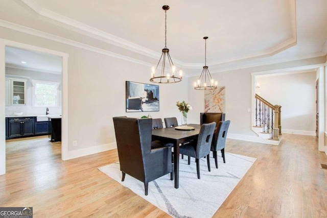 dining area with an inviting chandelier, a tray ceiling, light hardwood / wood-style flooring, crown molding, and sink