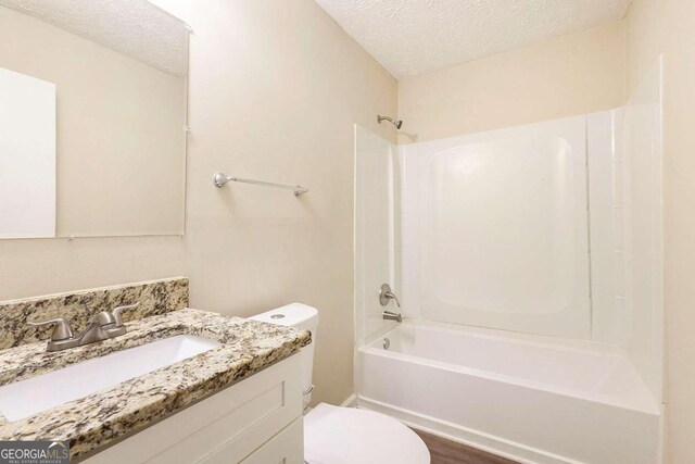 full bathroom featuring washtub / shower combination, a textured ceiling, toilet, vanity, and hardwood / wood-style flooring