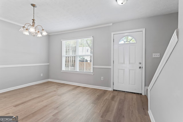 foyer entrance featuring a healthy amount of sunlight, ornamental molding, a textured ceiling, and light wood-type flooring