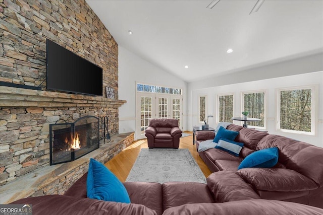 living room featuring high vaulted ceiling, wood finished floors, a stone fireplace, and recessed lighting