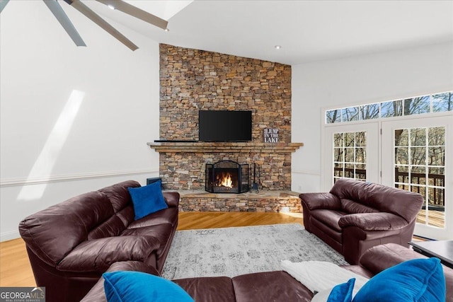 living area featuring a stone fireplace, ceiling fan, wood finished floors, and high vaulted ceiling