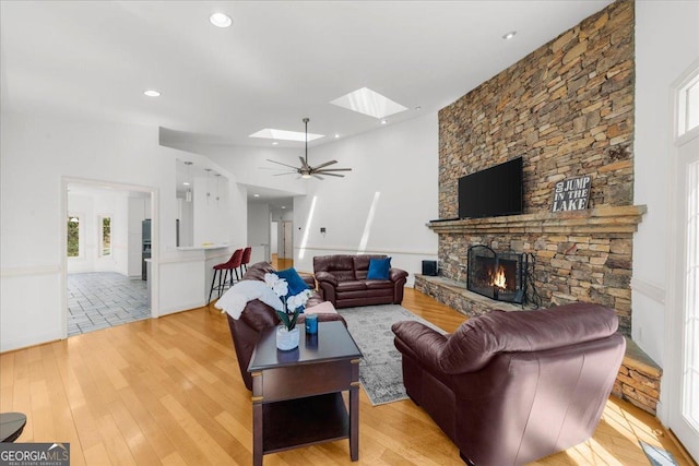 living area with light wood-style flooring, a ceiling fan, recessed lighting, a skylight, and a fireplace