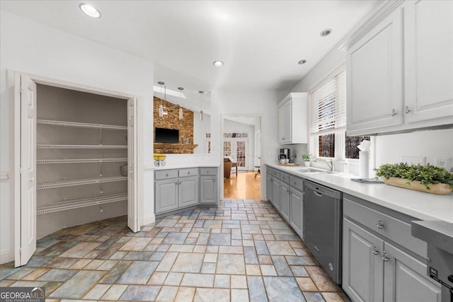 kitchen with gray cabinetry, stone finish floor, a sink, light countertops, and dishwasher