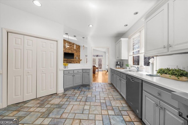 kitchen with gray cabinets, a sink, light countertops, stone finish flooring, and stainless steel dishwasher