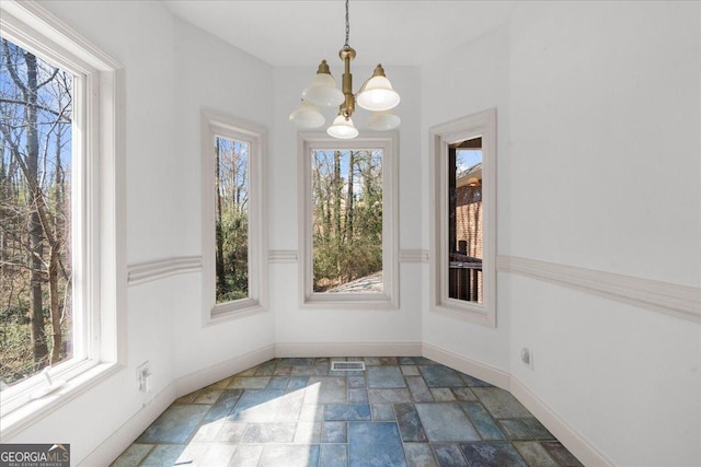 unfurnished dining area featuring visible vents, baseboards, an inviting chandelier, and stone tile flooring