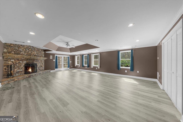 unfurnished living room featuring ornamental molding, a ceiling fan, a stone fireplace, light wood finished floors, and baseboards