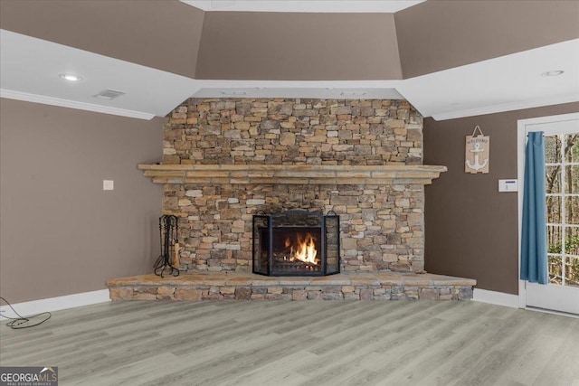 unfurnished living room with visible vents, wood finished floors, a stone fireplace, and ornamental molding