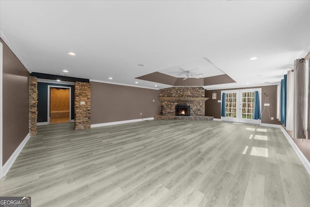 unfurnished living room with crown molding, baseboards, ceiling fan, light wood-type flooring, and a stone fireplace