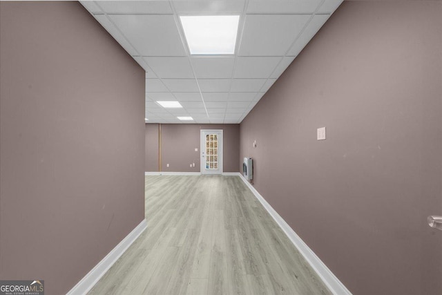 hall with a drop ceiling, light wood-style floors, and baseboards