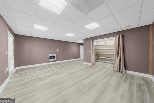 below grade area featuring heating unit, a paneled ceiling, baseboards, and wood finished floors