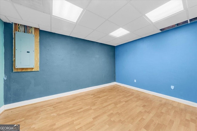 empty room with electric panel, wood finished floors, baseboards, and a drop ceiling