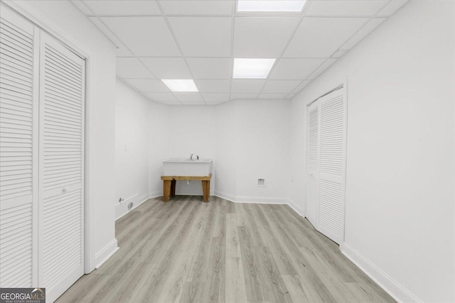 basement with light wood-style flooring, a paneled ceiling, and baseboards