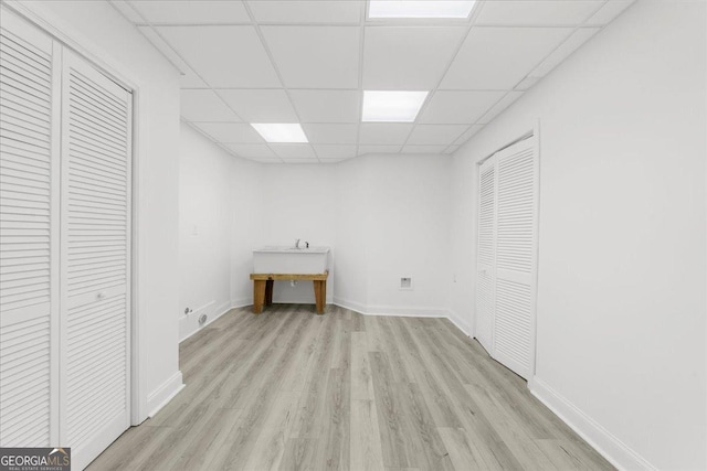 below grade area with a paneled ceiling, light wood finished floors, and baseboards