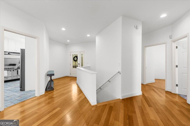 hall with light wood-style flooring, baseboards, recessed lighting, and an upstairs landing