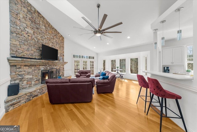 living area with light wood-type flooring, plenty of natural light, a stone fireplace, and ceiling fan