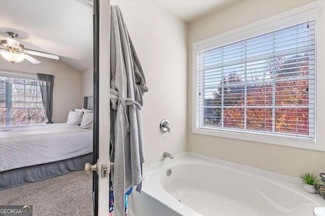 bathroom with a wealth of natural light, vaulted ceiling, ceiling fan, and a bathing tub