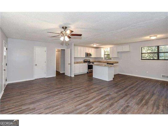 kitchen featuring a center island, white cabinetry, appliances with stainless steel finishes, a textured ceiling, and dark hardwood / wood-style flooring