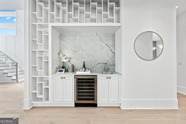 bar featuring white cabinets, sink, beverage cooler, and light hardwood / wood-style flooring