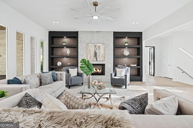 living room with ceiling fan, light wood-type flooring, built in features, and a premium fireplace