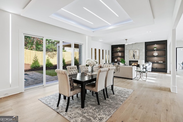 dining space featuring a tray ceiling, built in features, a high end fireplace, and light wood-type flooring