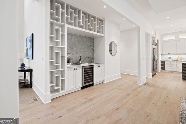 bar with backsplash, light hardwood / wood-style flooring, white cabinets, wine cooler, and built in fridge