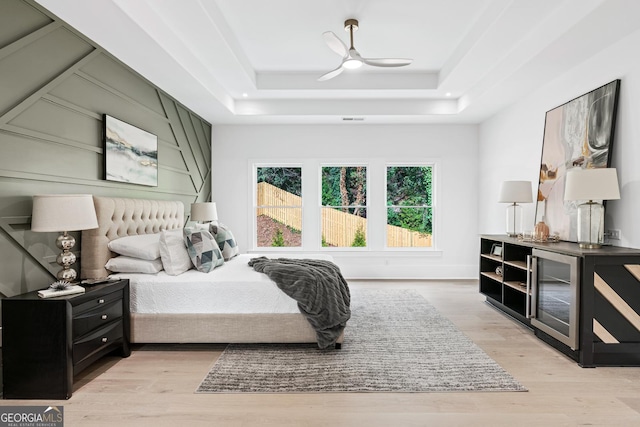 bedroom with light wood-type flooring, a raised ceiling, and ceiling fan