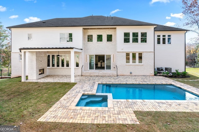 rear view of house featuring a lawn, a pool with hot tub, a patio area, and an outdoor fireplace