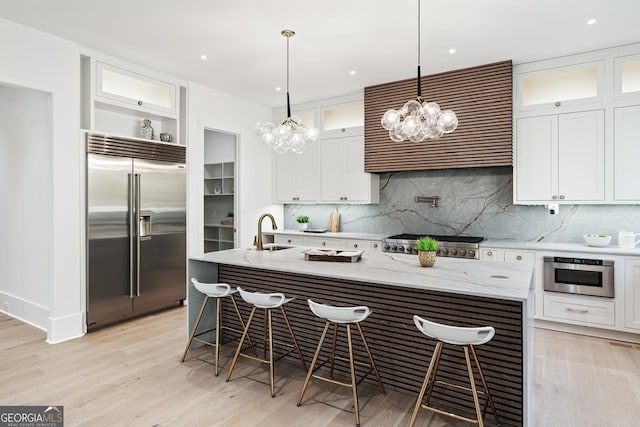 kitchen with light stone counters, a kitchen island with sink, a breakfast bar, white cabinets, and appliances with stainless steel finishes