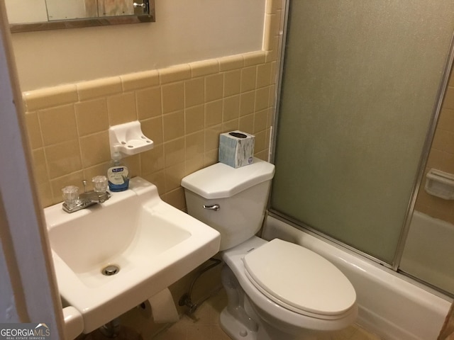 full bathroom with enclosed tub / shower combo, toilet, sink, and tile walls