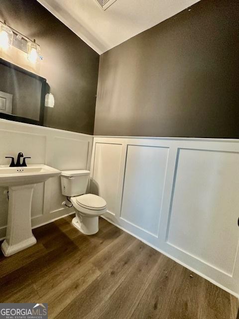 bathroom featuring a decorative wall, wood finished floors, toilet, and a wainscoted wall