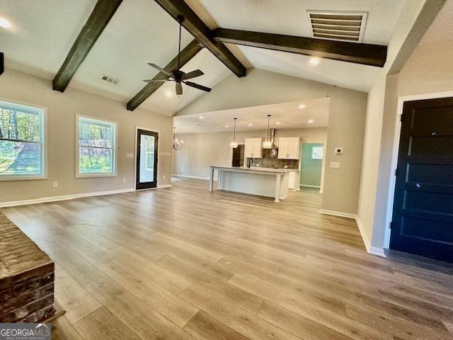 unfurnished living room featuring light wood-style flooring, beam ceiling, a ceiling fan, baseboards, and high vaulted ceiling