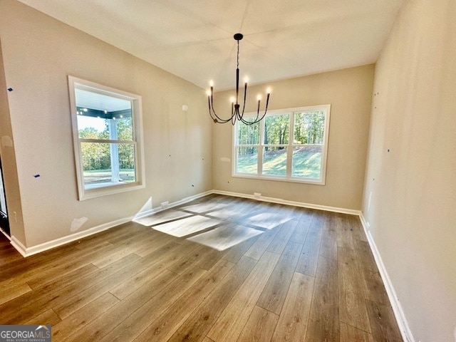 unfurnished dining area featuring a wealth of natural light, wood-type flooring, and an inviting chandelier