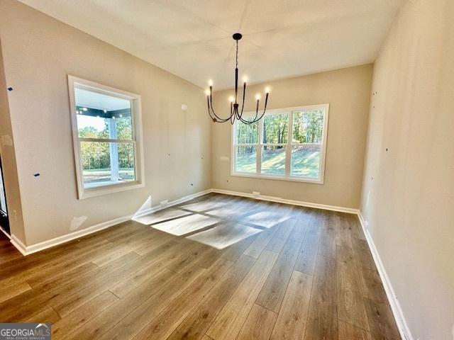 unfurnished dining area featuring dark wood-style floors, a chandelier, and baseboards