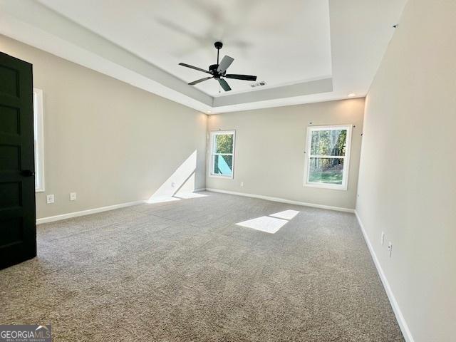 spare room with a tray ceiling, carpet floors, ceiling fan, and baseboards