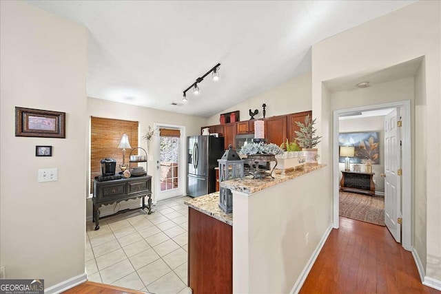 kitchen with lofted ceiling, stainless steel refrigerator with ice dispenser, light stone countertops, kitchen peninsula, and light wood-type flooring