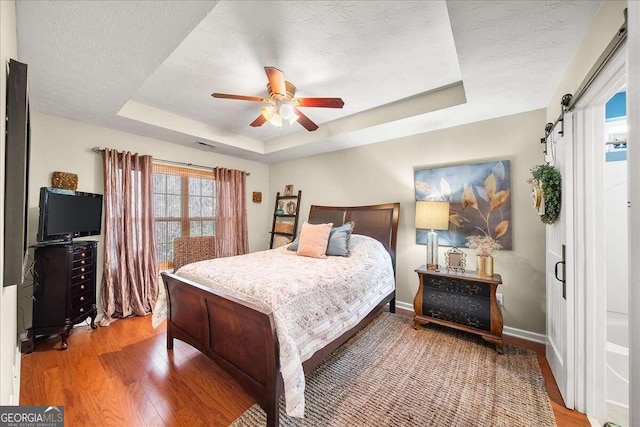 bedroom with hardwood / wood-style flooring, a tray ceiling, a barn door, and a textured ceiling