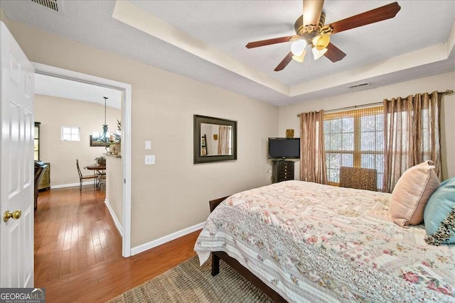 bedroom with dark wood-type flooring, ceiling fan, and a tray ceiling