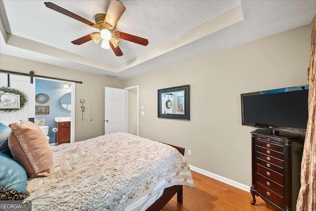 bedroom featuring a textured ceiling, a tray ceiling, hardwood / wood-style flooring, ceiling fan, and a barn door