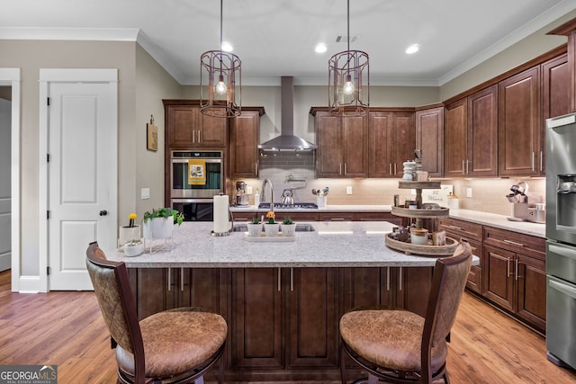 kitchen featuring a kitchen bar, pendant lighting, stainless steel appliances, and wall chimney range hood