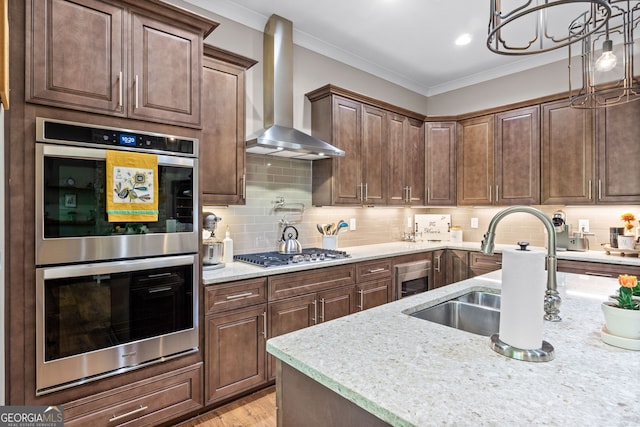 kitchen with tasteful backsplash, stainless steel appliances, wall chimney range hood, pendant lighting, and a chandelier