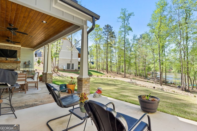 view of patio / terrace featuring ceiling fan, a water view, and exterior fireplace